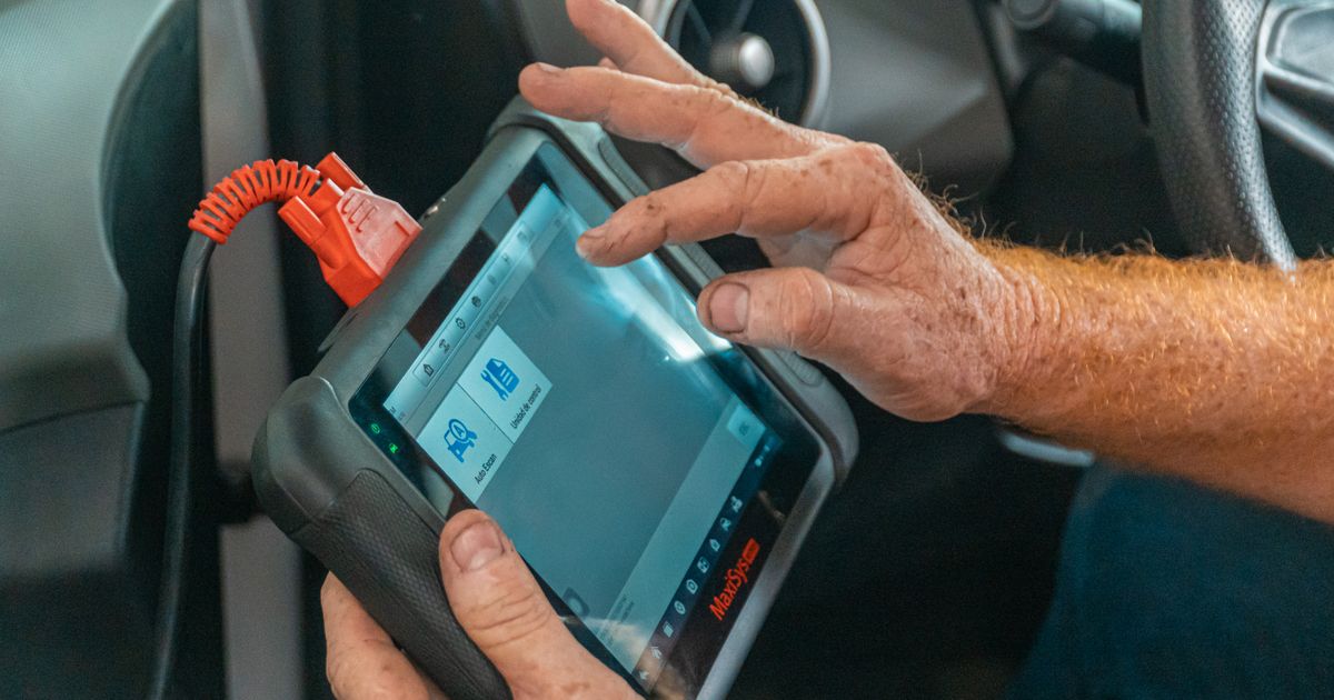 Mechanic using a handheld diagnostic scanner inside a car