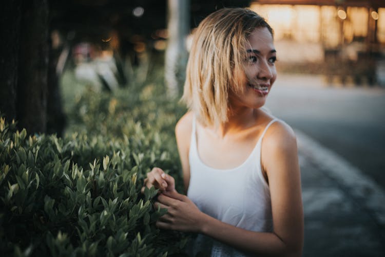 Woman Touching The Hedge, Looking Over Shoulder And Smiling 