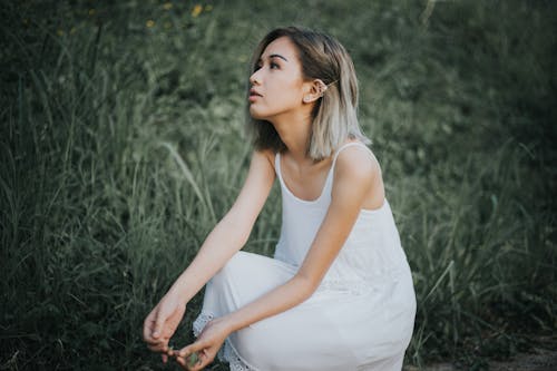 Woman in White Tank Dress Sitting on Grass Field