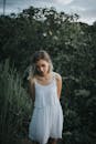 一名身穿白色连衣裙的女子安静地站在户外，周围环绕着郁郁葱葱的绿色植物