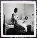 Aged photography of man lying on bed in hospital bed with woman sitting nearby