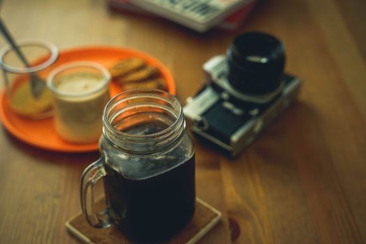 Moody close-up of coffee in a jar alongside a vintage camera on a rustic wooden table.