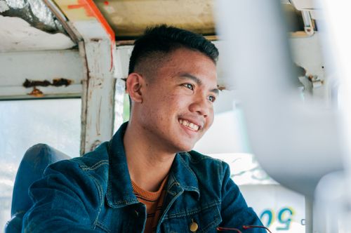 Free Low angle of cheerful Asian male in denim shirt sitting in weathered public transport smiling away Stock Photo