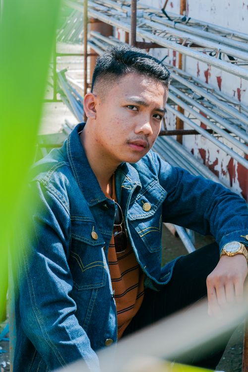 Free Casual Asian man in denim jacket looking at camera sitting in sunny yard Stock Photo