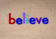 “相信”一词的排版充满活力、丰富多彩，背景是粗麻布纹理