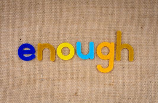 Bright felt letters spell 'enough' on a textured burlap background, offering inspiration.
