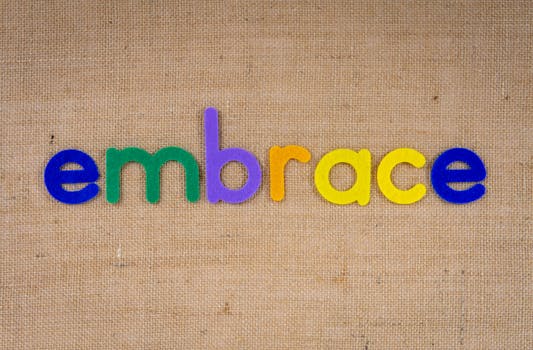 在自然纹理的织物背景上，五颜六色的毛毡字母拼写出“拥抱”