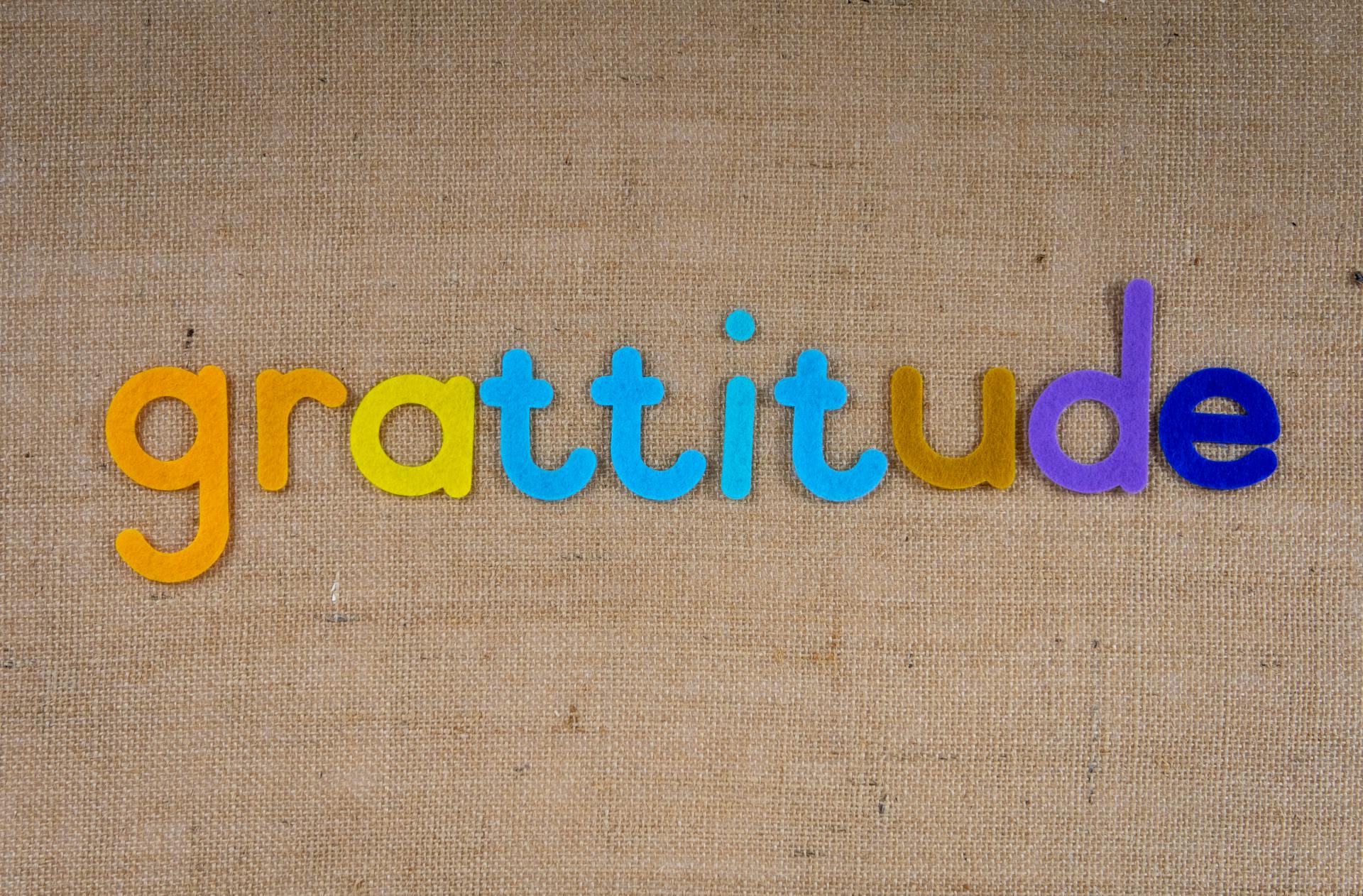 Vibrant colored letters spelling 'gratitude' on a textured burlap surface.
