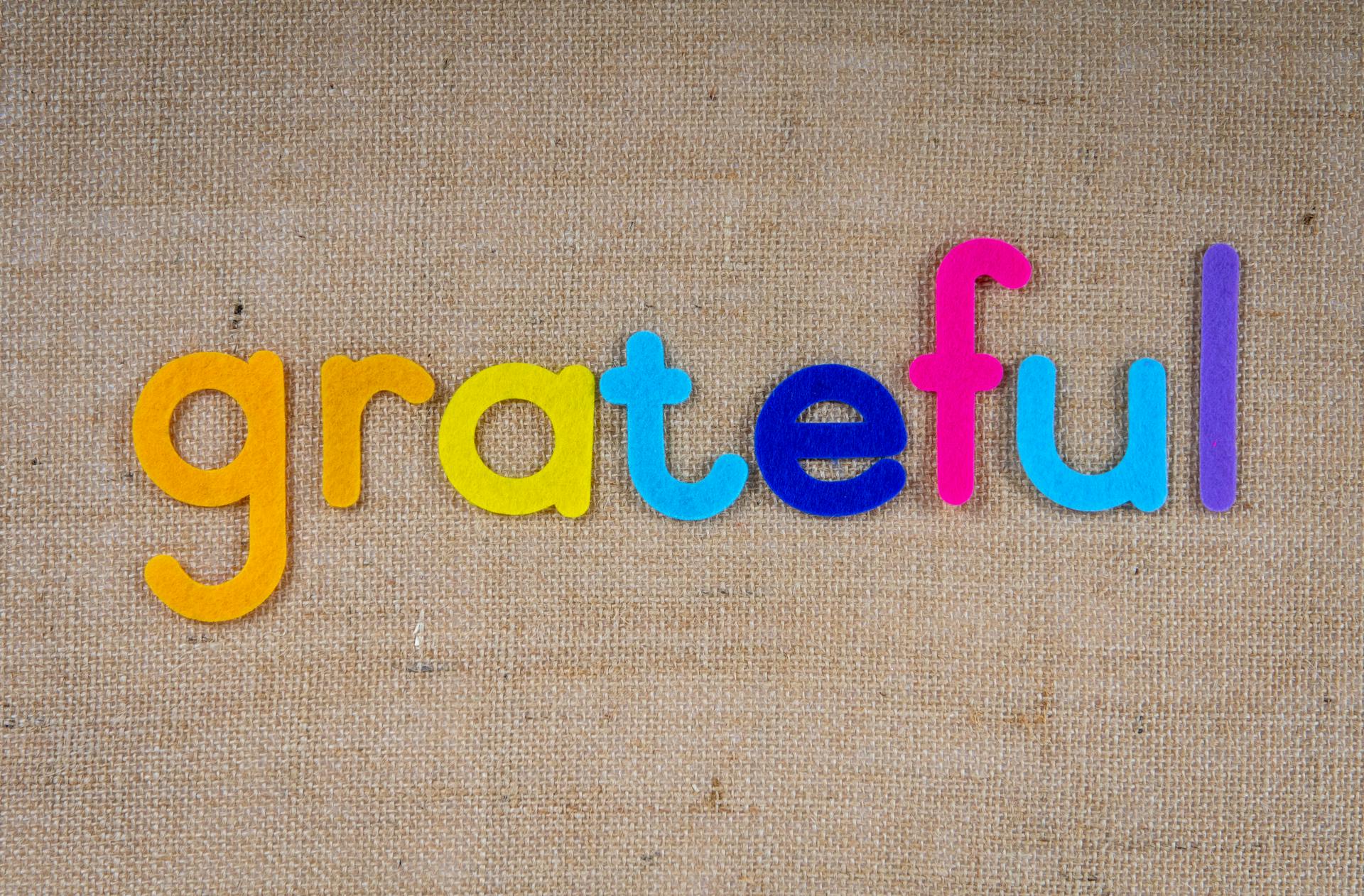 Colorful felt letters forming the word 'grateful' on a burlap background.