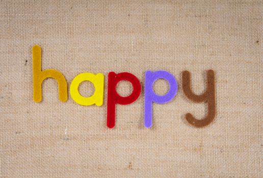 Colorful felt letters spell 'happy' on a burlap background. Cheerful and crafty.