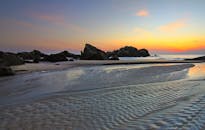 岩石海岸上，温柔的沙波纹与宁静的海浪间，一轮日出静谧升起