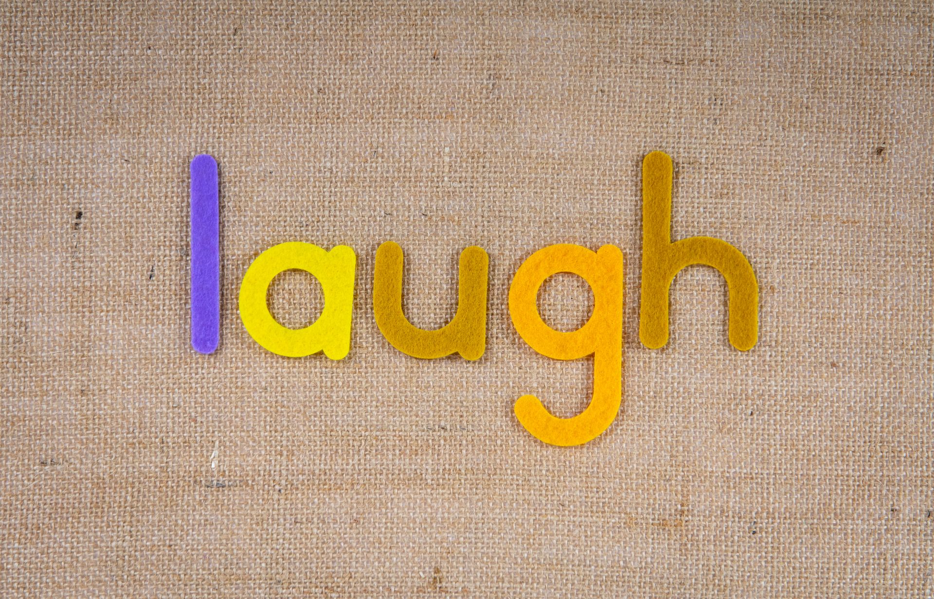 The word 'laugh' in colorful felt letters on a burlap background provides a cheerful and textured look.