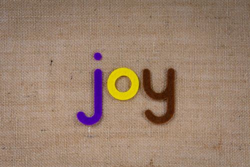 Free Colorful felt letters spelling 'joy' on a textured burlap background. Stock Photo