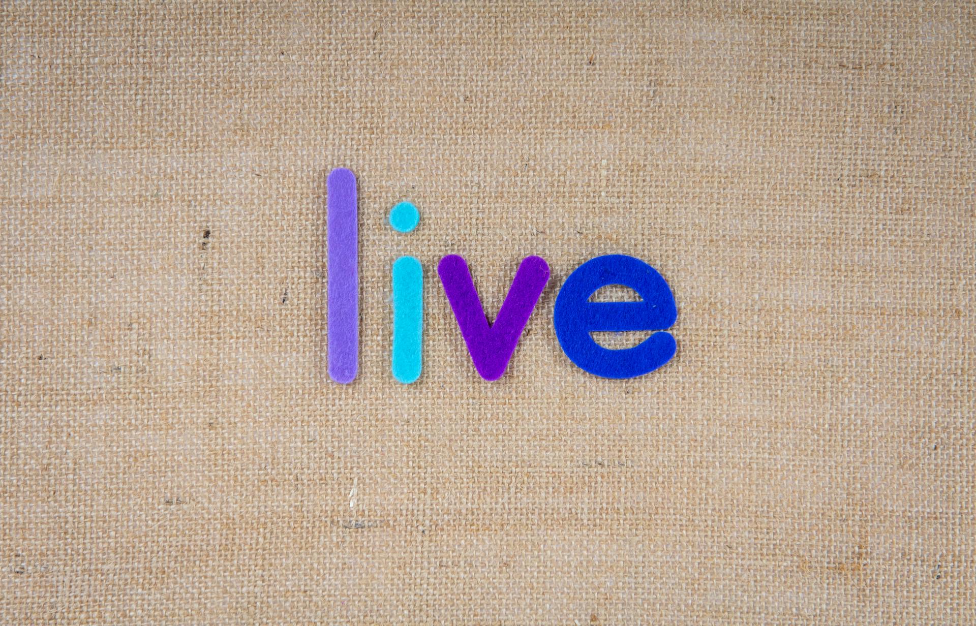 Colorful letters spelling 'live' on a burlap textured background, inspiring and artistic.