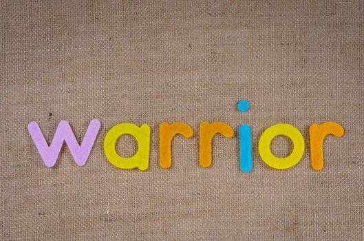 Vivid felt letters spelling 'warrior' on a textured burlap background