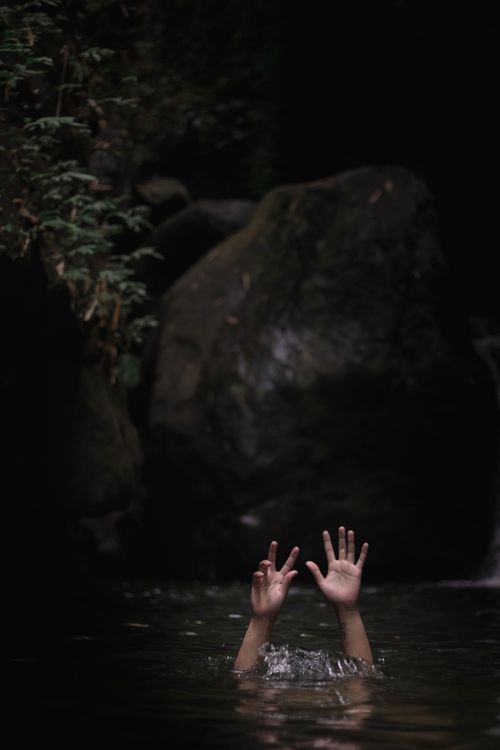 Free Hands reaching out of water surrounded by rocks, evoking a surreal and moody atmosphere. Stock Photo