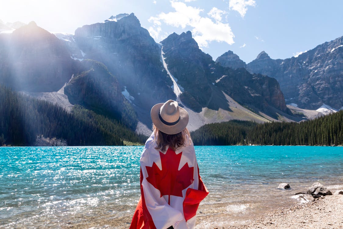 Free Person With A Canadian Flag Around Her Standing Near Lake Stock Photo