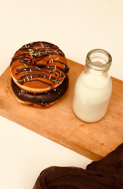 Free Tasty chocolate doughnuts with colorful sprinkles beside a glass of milk on a wooden board. Stock Photo