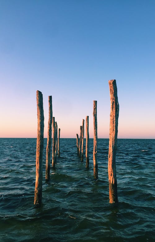 Poles of remained pier sticking out of calm rippling water against dusky sky