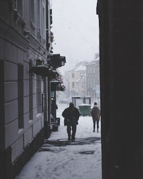 A man walking alone on a snowy, foggy street during a cold winter day.