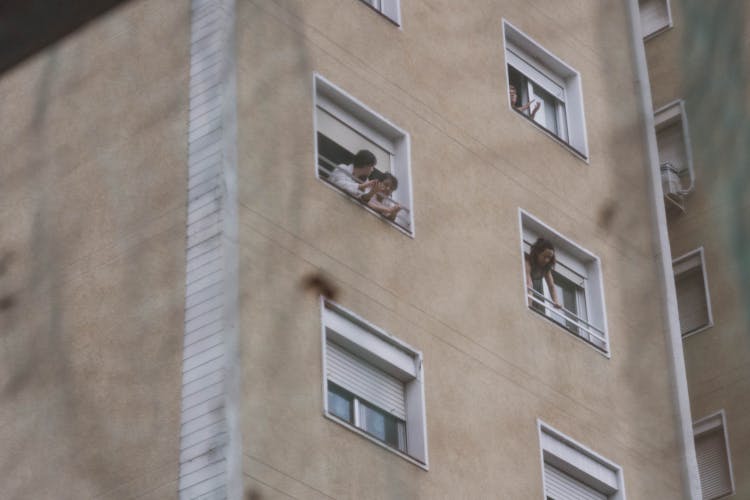 People Looking Out Of Their Windows In A Block Of Flats