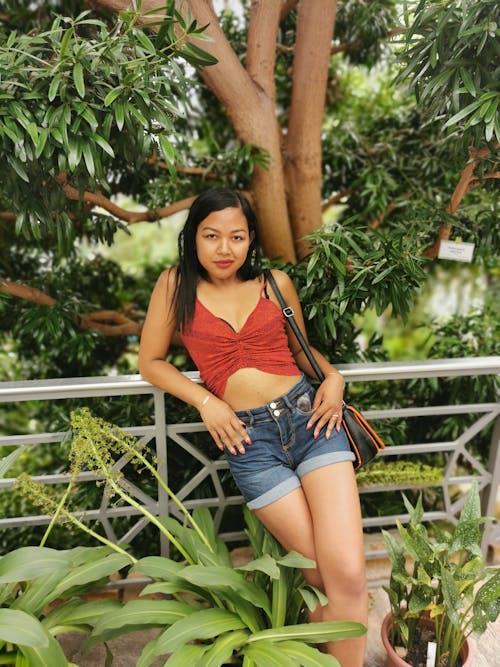 Woman Wearing Red Crop Top and Blue Denim Shorts While Leaning on Metal Railings