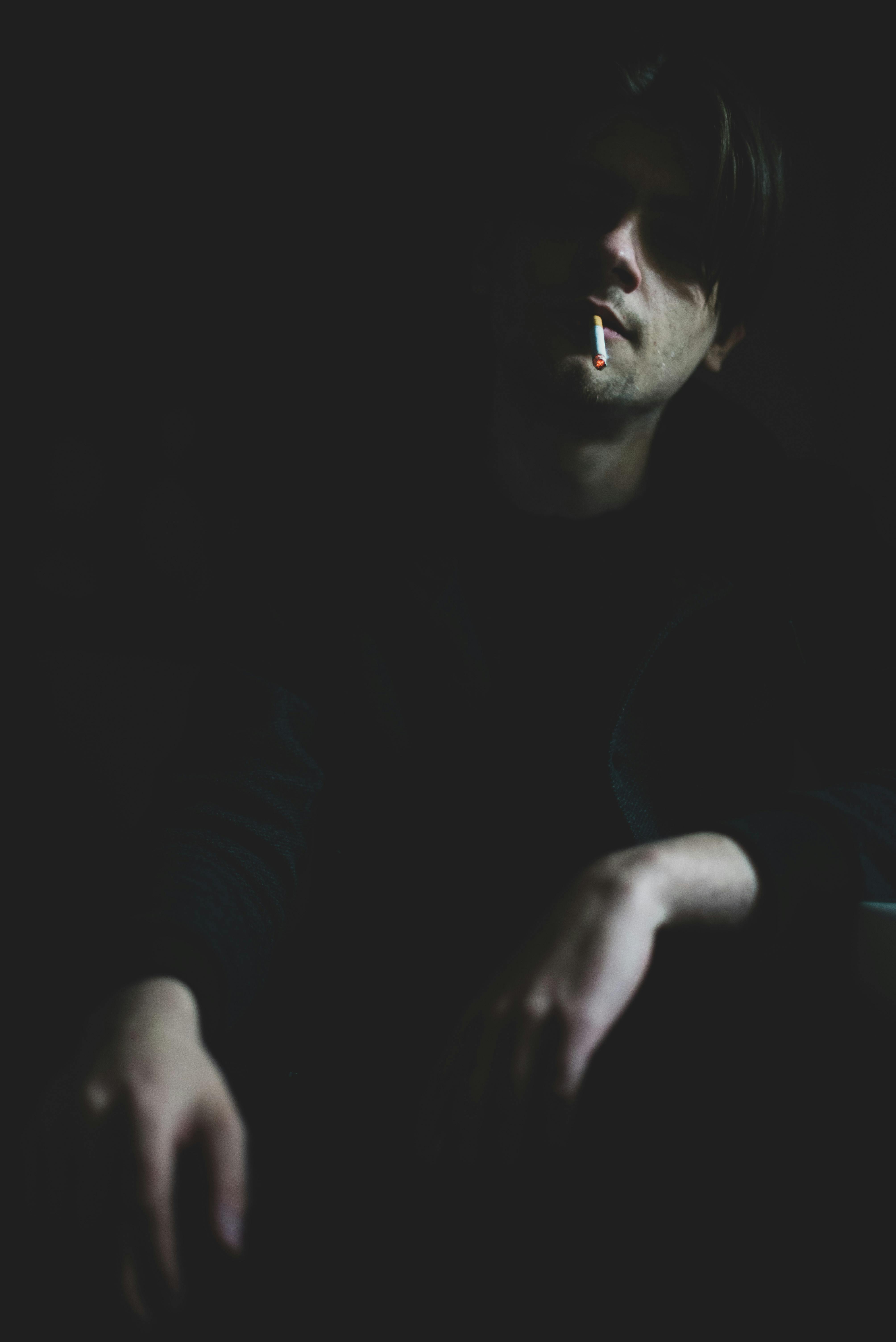 Dark moody portrait of a man smoking in dim lighting, highlighting the cigarette.