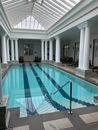 Clear pool under glass roof in spacious villa hall with colonnade in daylight