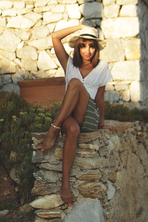 Free A Woman in a Sun Hat Sitting on a Rock Wall Stock Photo