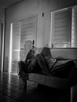 Black and white image featuring ghostly silhouette on a sofa indoors, capturing a surreal and moody atmosphere.