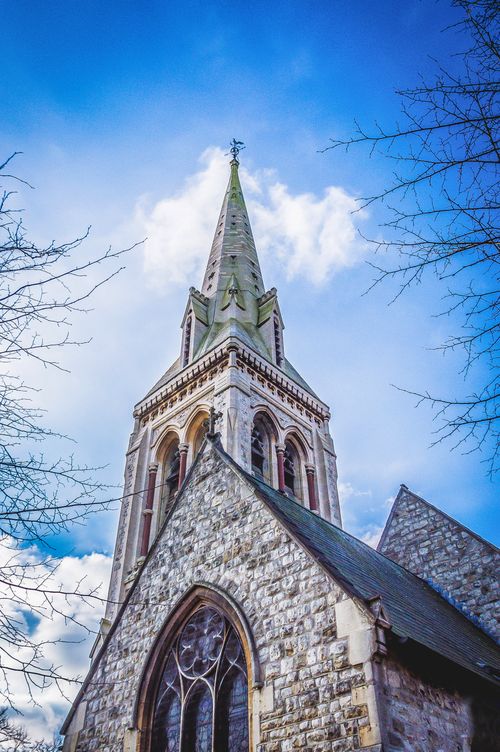 Free A stunning view of a Gothic cathedral's tower under a vibrant blue sky with scattered clouds. Stock Photo