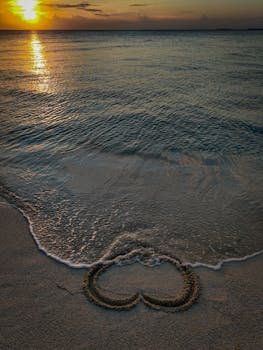 Heart drawn in sand at Maldives beach during sunset, capturing romance and tranquility.