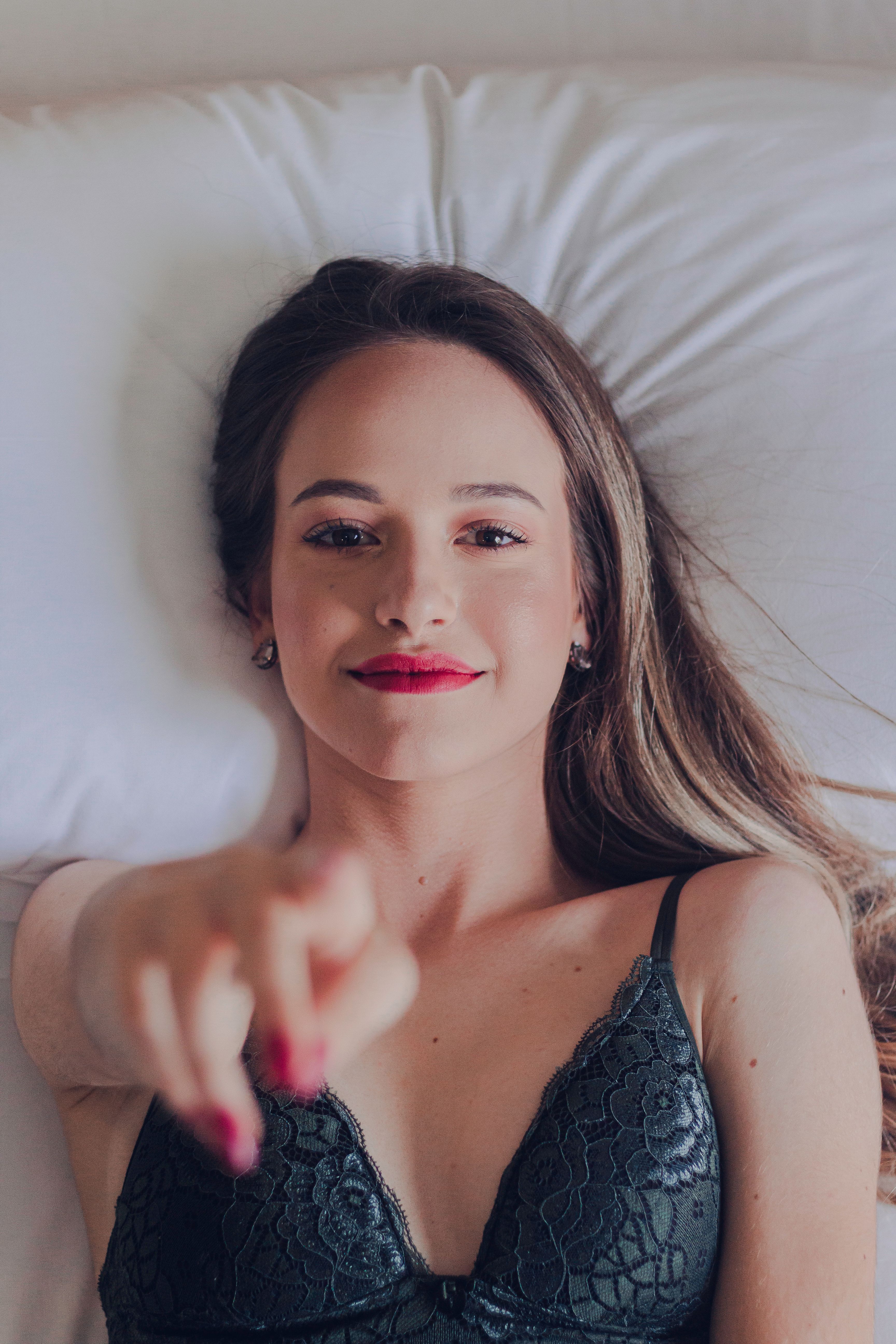 Top view of sexy young female in underwear lying on bed and pointing at camera