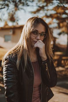 Stylish portrait of a blonde woman in a leather jacket on a sunny day outdoors.