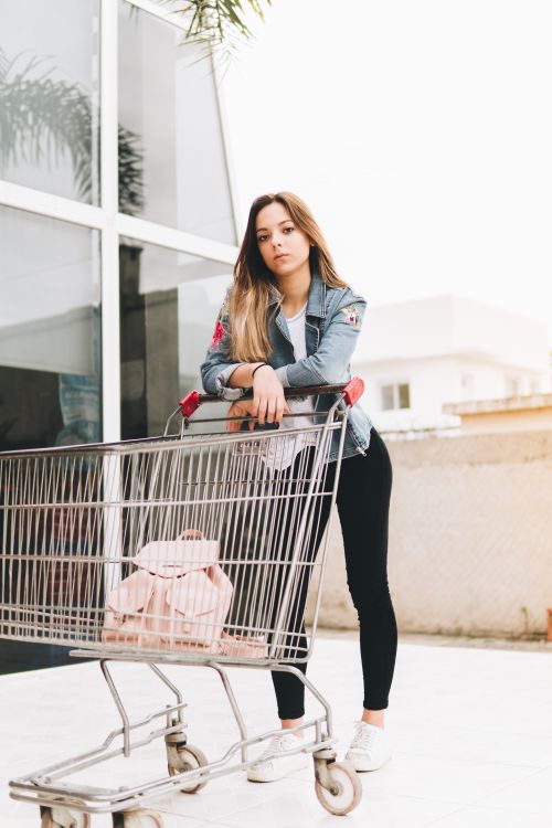 Free Fashionable young woman posing with a shopping cart outside a store. Stock Photo