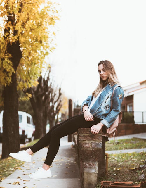 Woman in Blue Denim Jacket and Black Pants Sitting on Brown Wooden Bench