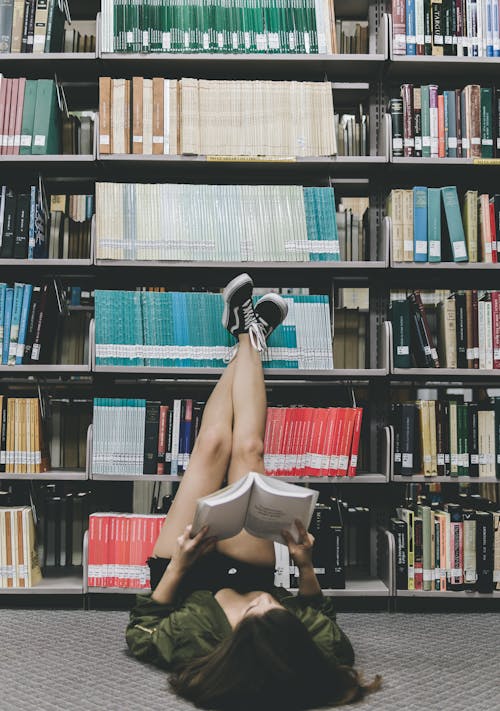 A Woman Reading a Book while lying on the Floor of a Library