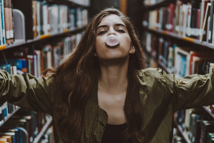 A Woman In A Green Jacket Blowing A Bubble