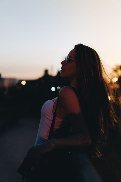 Free Profile silhouette of a woman in sunglasses leaning against a railing during a sunset. Stock Photo