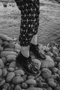 From above side view black and white of crop unrecognizable trendy female in trousers with ornament and leather footwear standing on stones near pond with rippled water