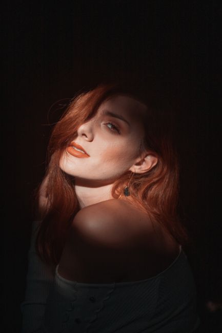 Striking portrait of a red-haired woman in moody lighting, highlighting her features.