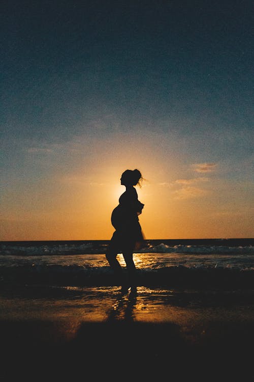 Unrecognizable pregnant woman on sea beach at colorful sunset