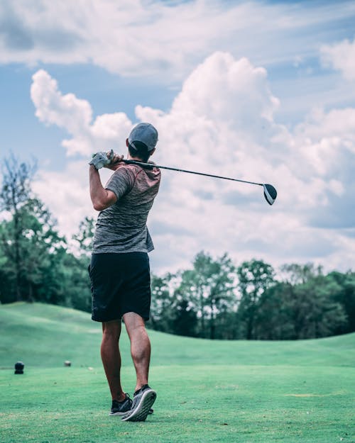 Unrecognizable golfer with golf club playing in field under sky