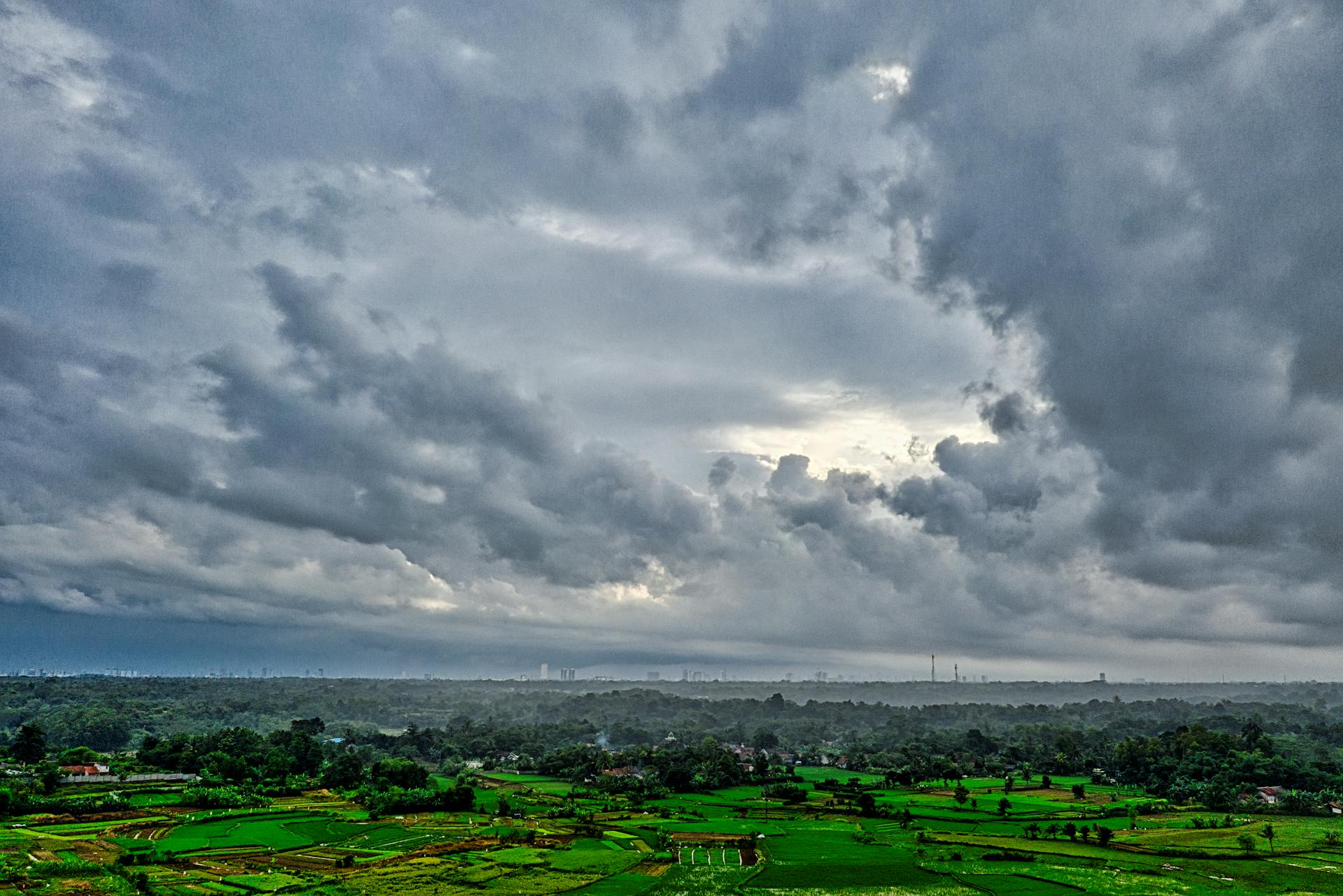 Aerial view of lush green fields under a dramatic overcast sky in Rumpin, West Java, Indonesia.