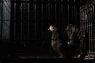 Side view of black hen with red comb and wattles with spiky beak standing in coop with metal fence in darkness