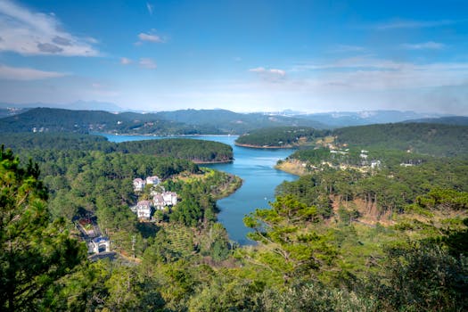 A breathtaking aerial view capturing a serene lake surrounded by lush forests and distant mountains under a clear blue sky.