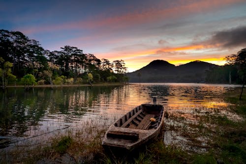 Old boat near lake and mountains under sky at sunset