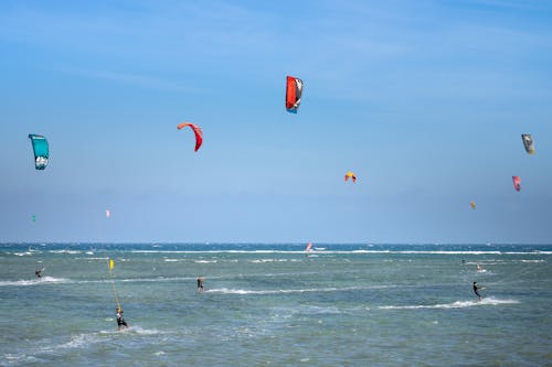 Free Anonymous people with kites surfing in waving sea under blue sky in summer sunny day Stock Photo