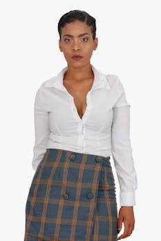Confident woman in a white blouse and plaid skirt, posing against a white background.