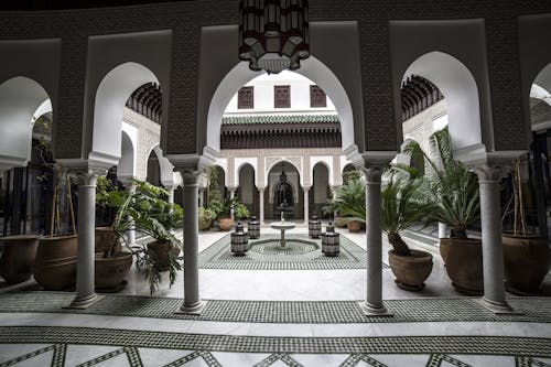 Beautiful oriental palace inner yard with arches and mosaic on floor decorated with lush potted plants and cozy fountain in center